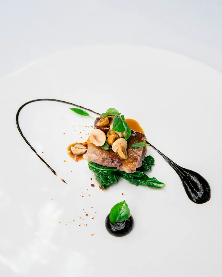Line-caught sea bass with spinach and a dark olive reduction on a white plate.