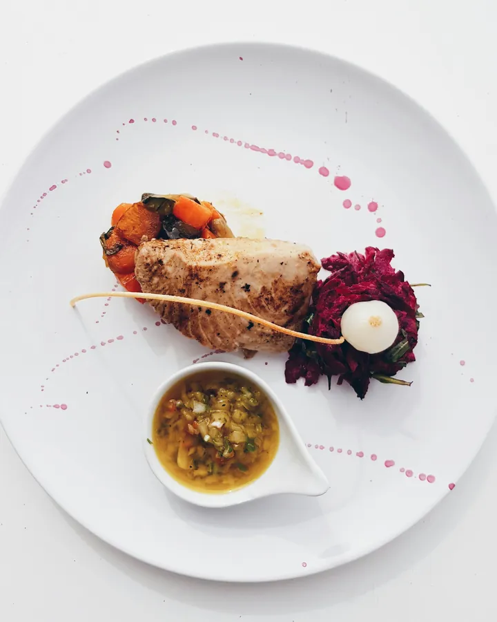 Cured fish with citrus and flowers arranged sparely on a wide white plate.