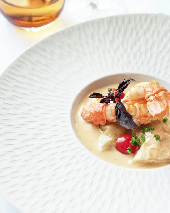 Langoustine in a pale bisque served in a fluted white bowl.