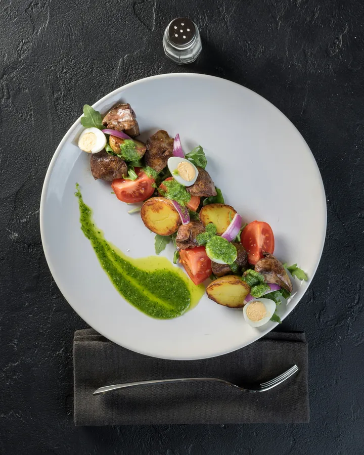 A white plate of grains, tomato and herb oil, seen from above on a dark stone table.
