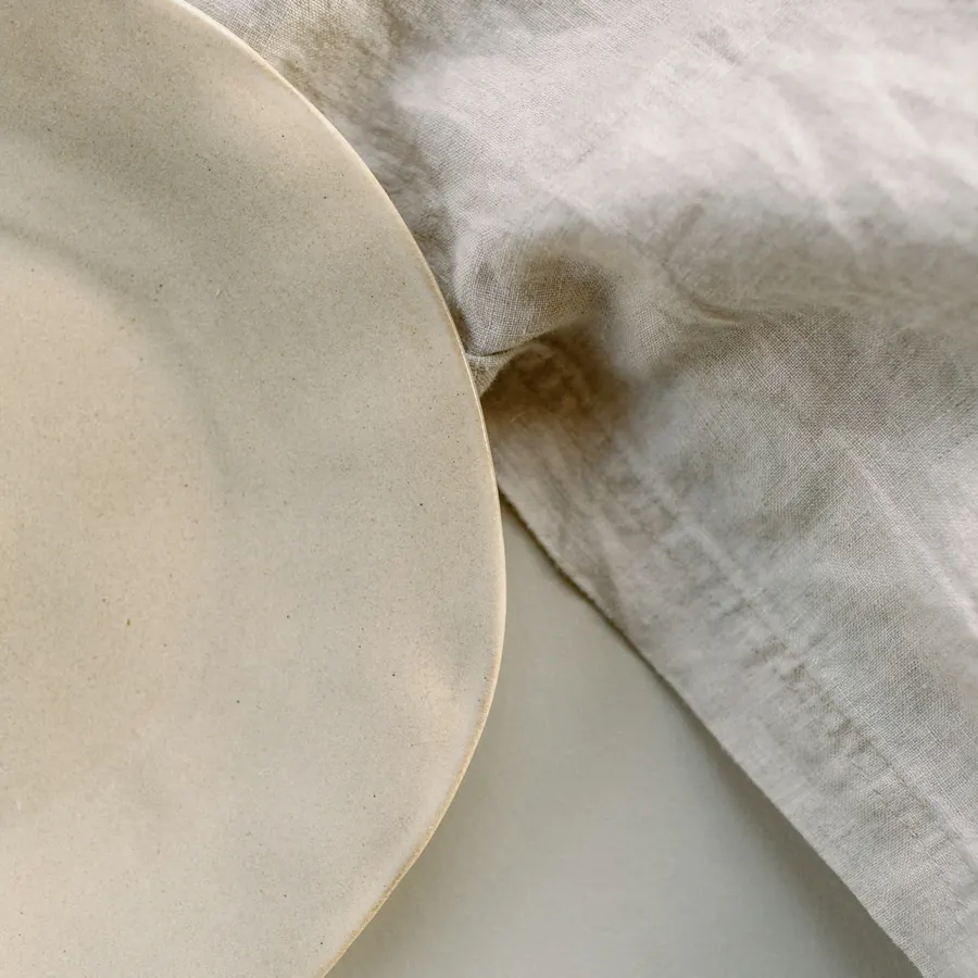 A hand-thrown stoneware plate resting on crumpled natural linen.