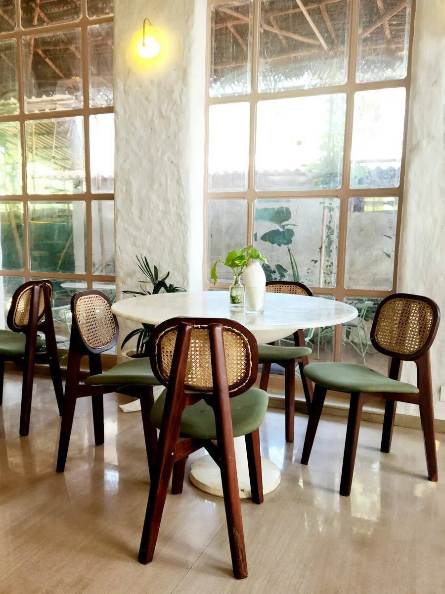 A limestone dining room with cane chairs and tall windows opening to a garden.