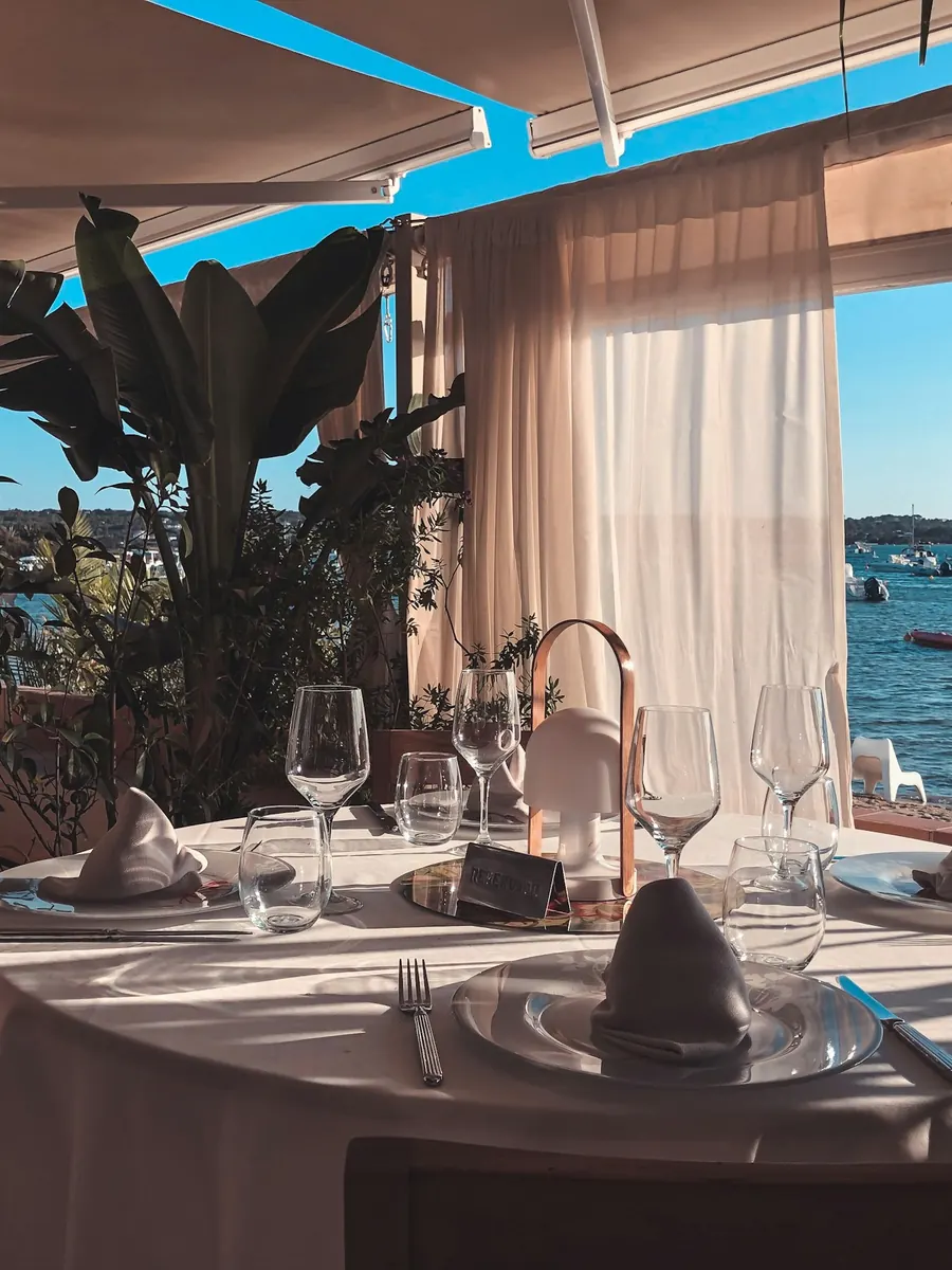 A shaded dining terrace of white linen and glassware opening onto the water.